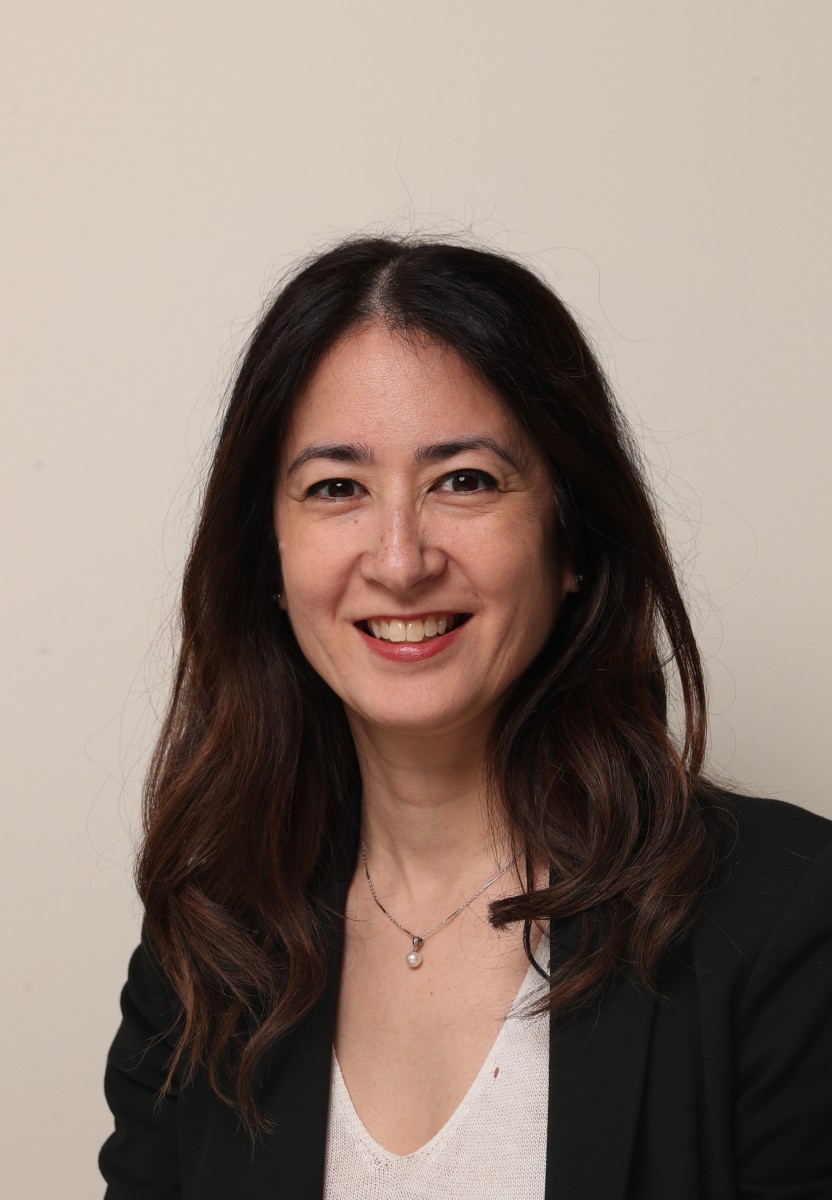 Image of Gail Hamamoto wearing a white shirt with a black blazer with a tan background.