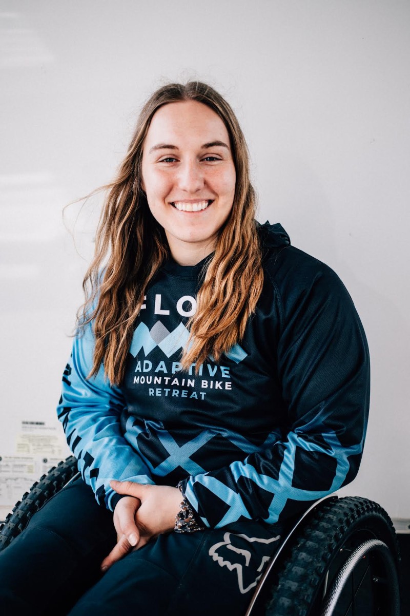 Image of Sierra Roth wearing a light blue and black Adaptive Mountain Bike Retreat sweater and black pants. Image has a white background.